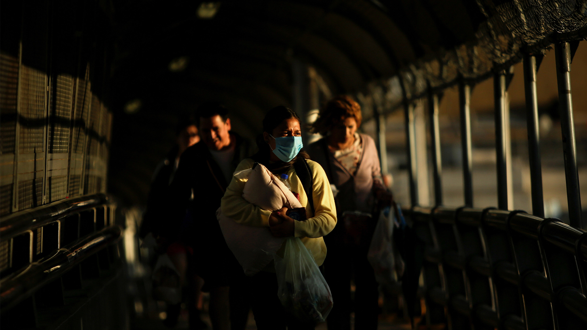 Woman wearing protective mask carries her baby across international border bridge at El Paso, Texas.